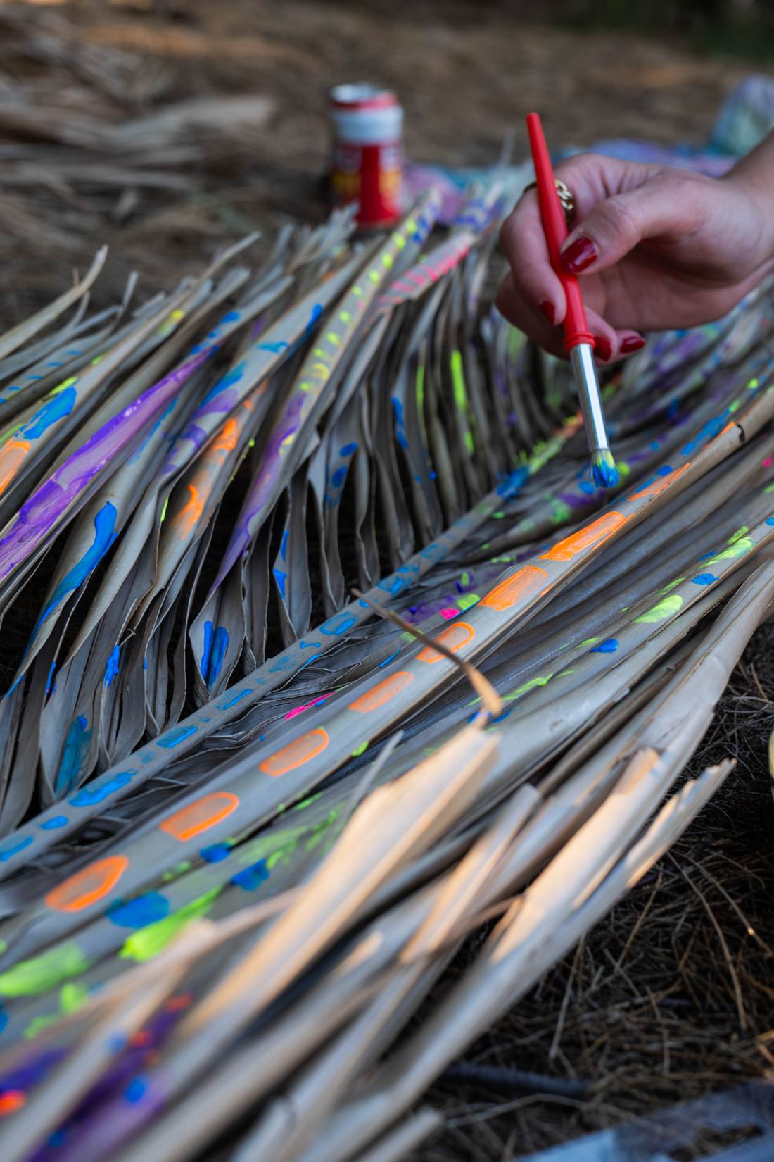 A hand painting bright patterns onto dried palm fronds