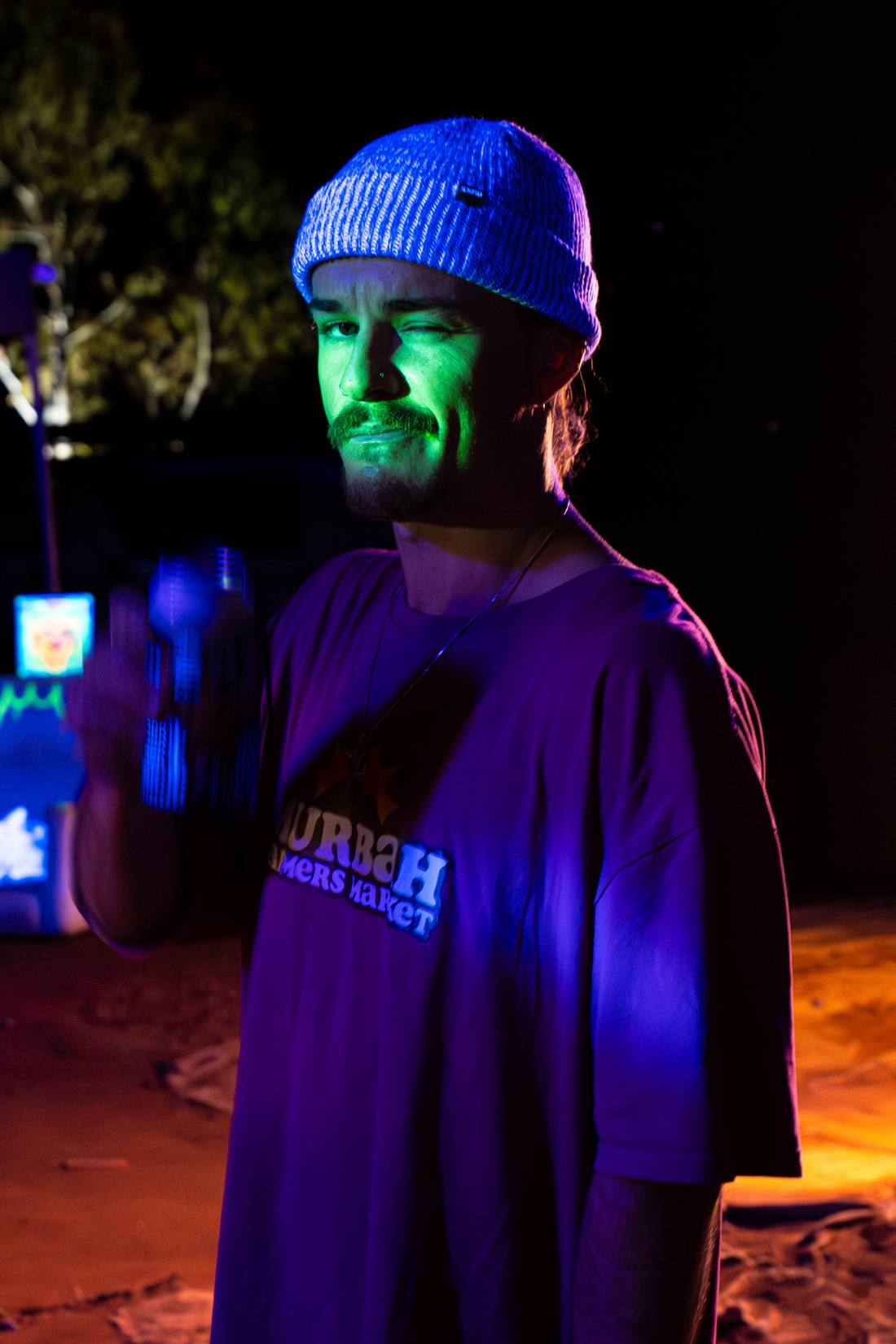 A festivalgoer in a knitted beanie winking beneath blue and green lights