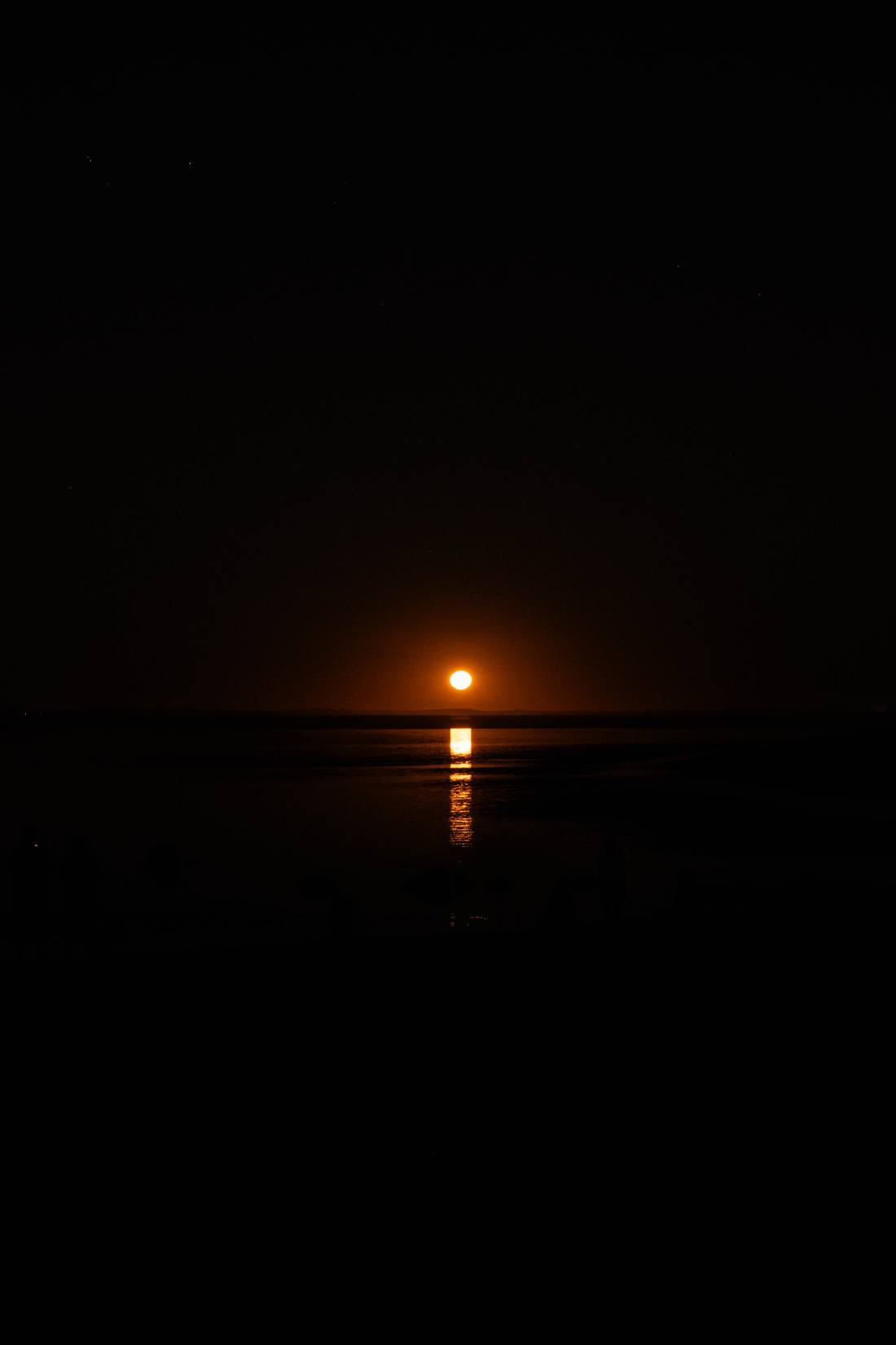 An orange moon rising over dark water with a bright reflection