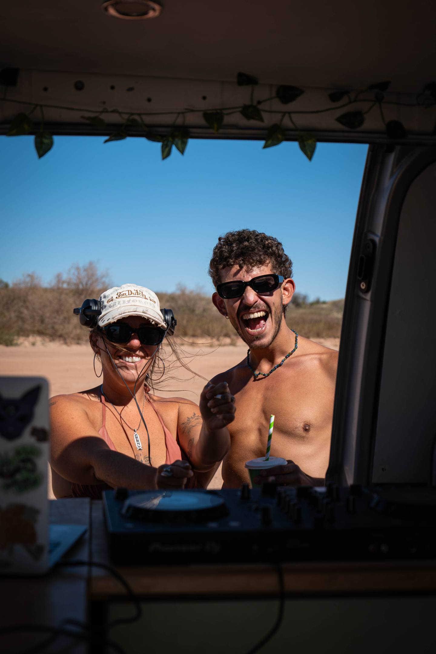 Two friends in sunglasses laughing through the open door of a campervan