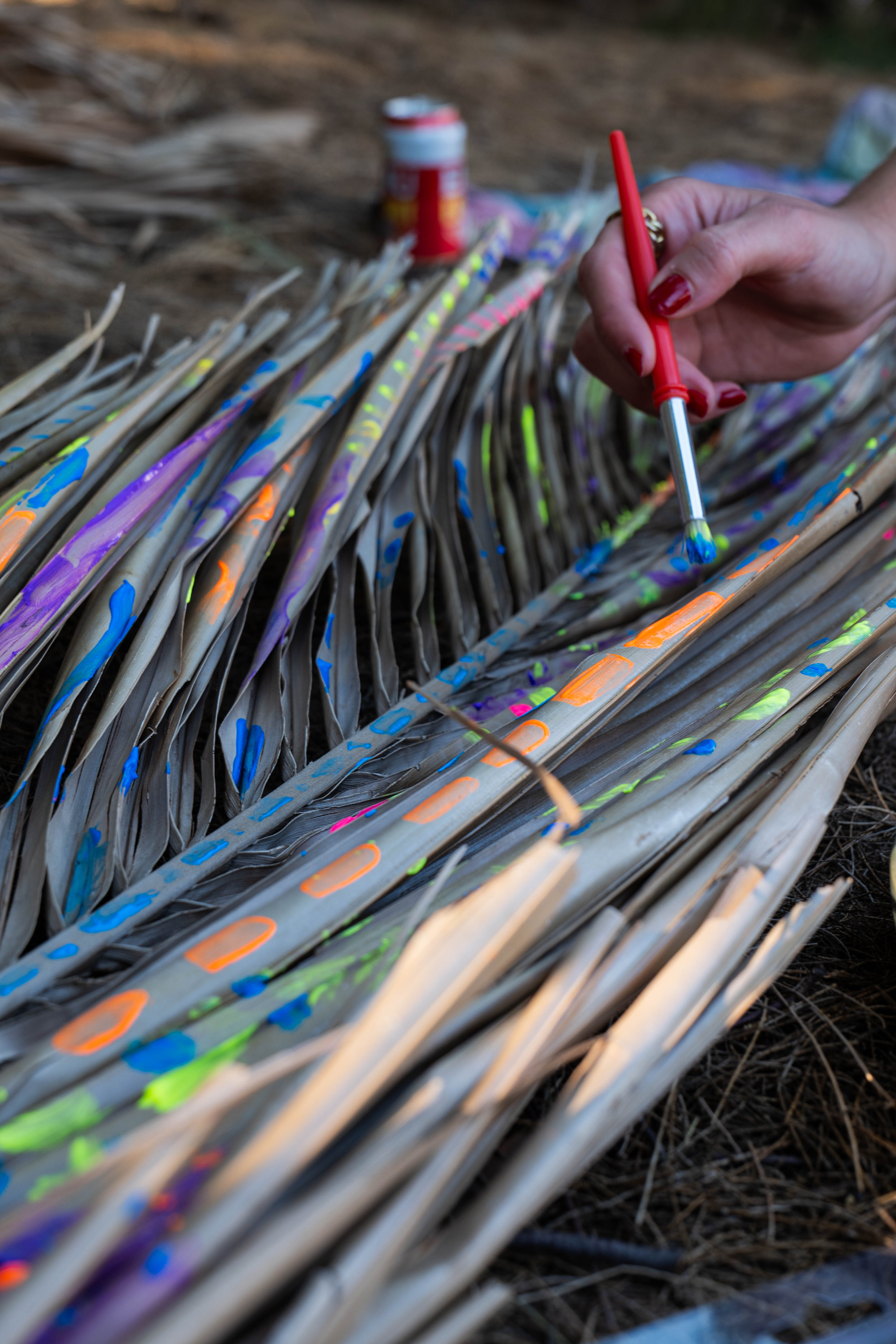 A hand painting bright patterns onto dried palm fronds