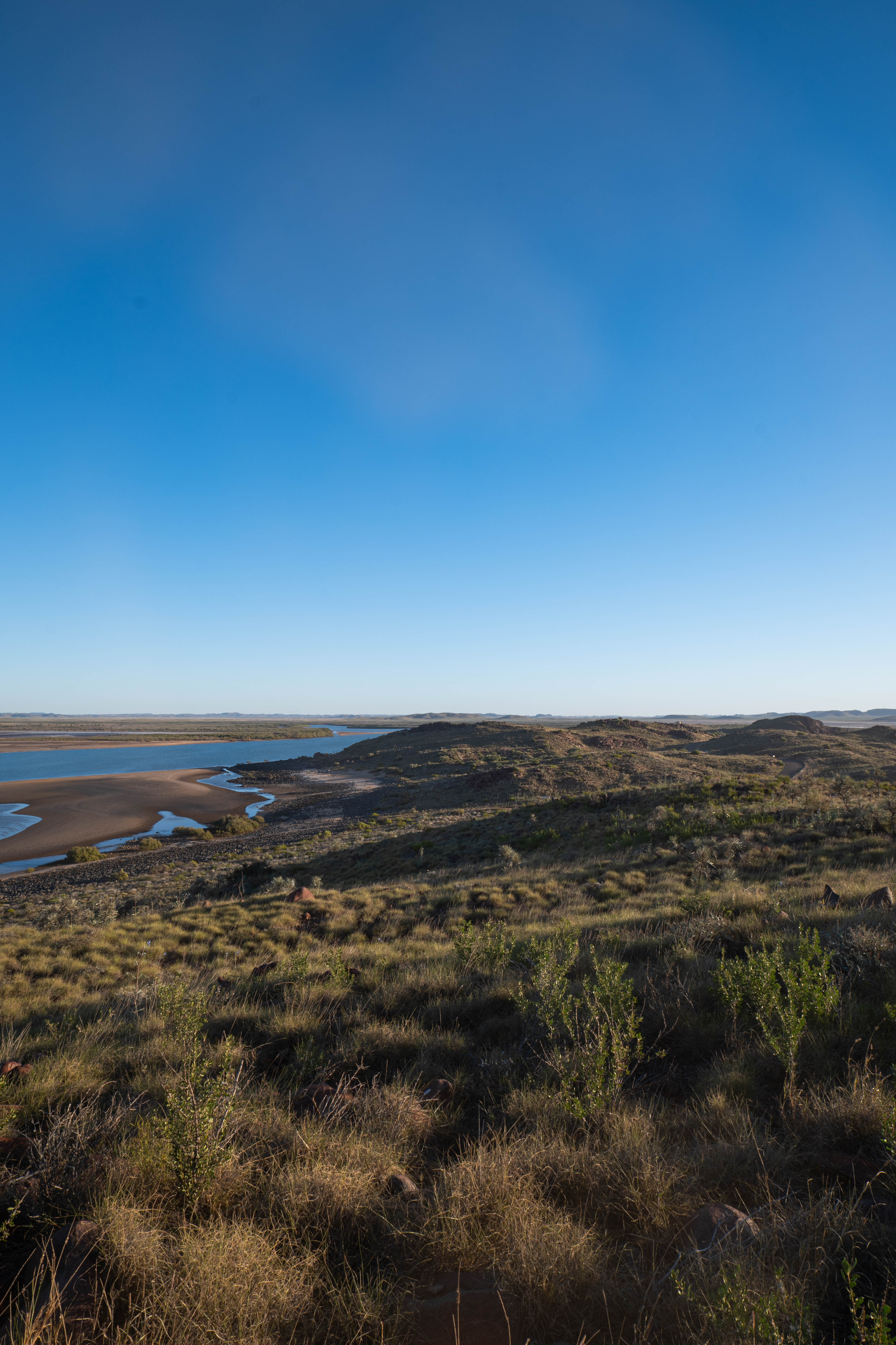 A broad Pilbara tidal inlet winding between low rocky hills beneath a clear blue sky