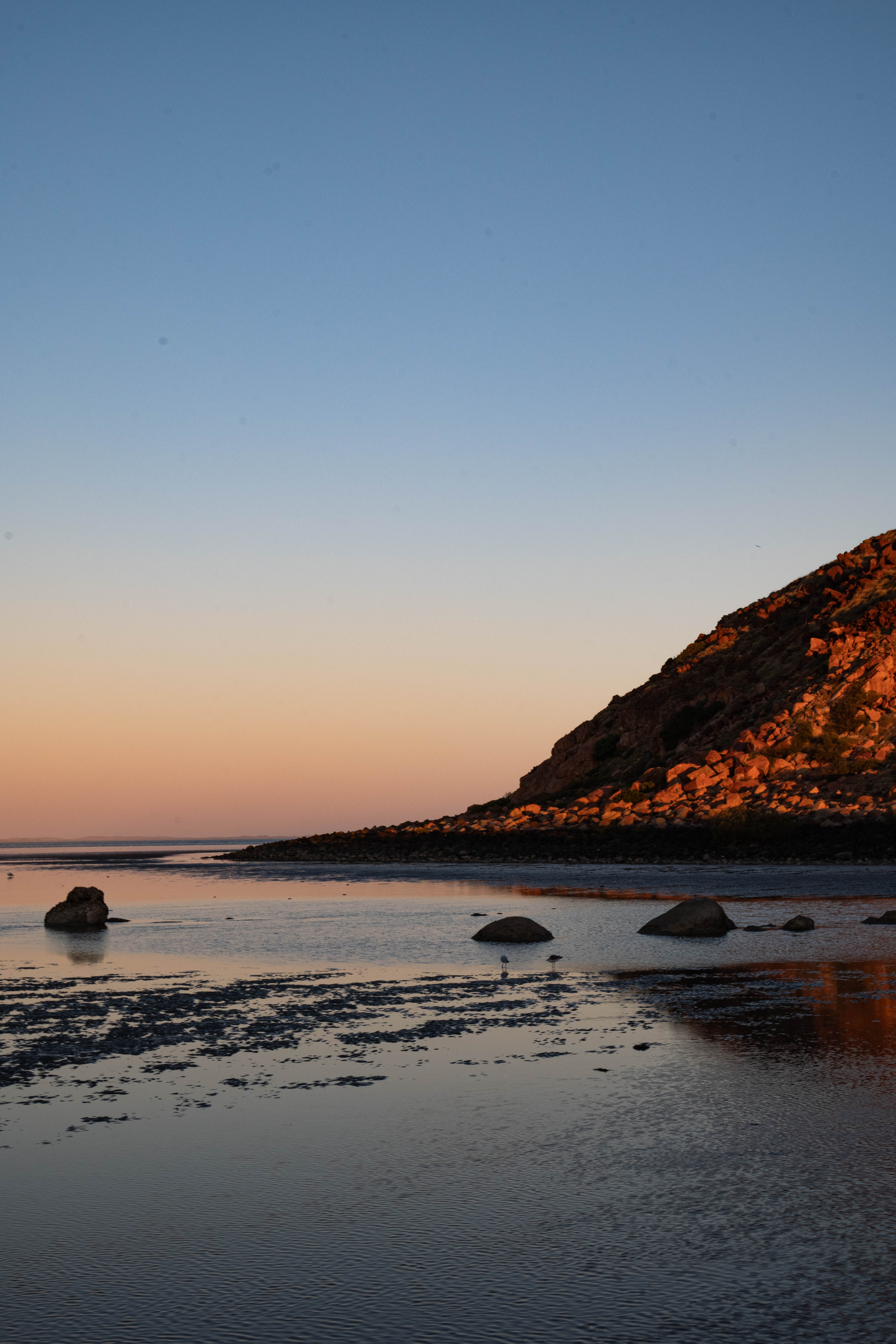 A red rocky Pilbara shoreline reflected in calm water at sunset