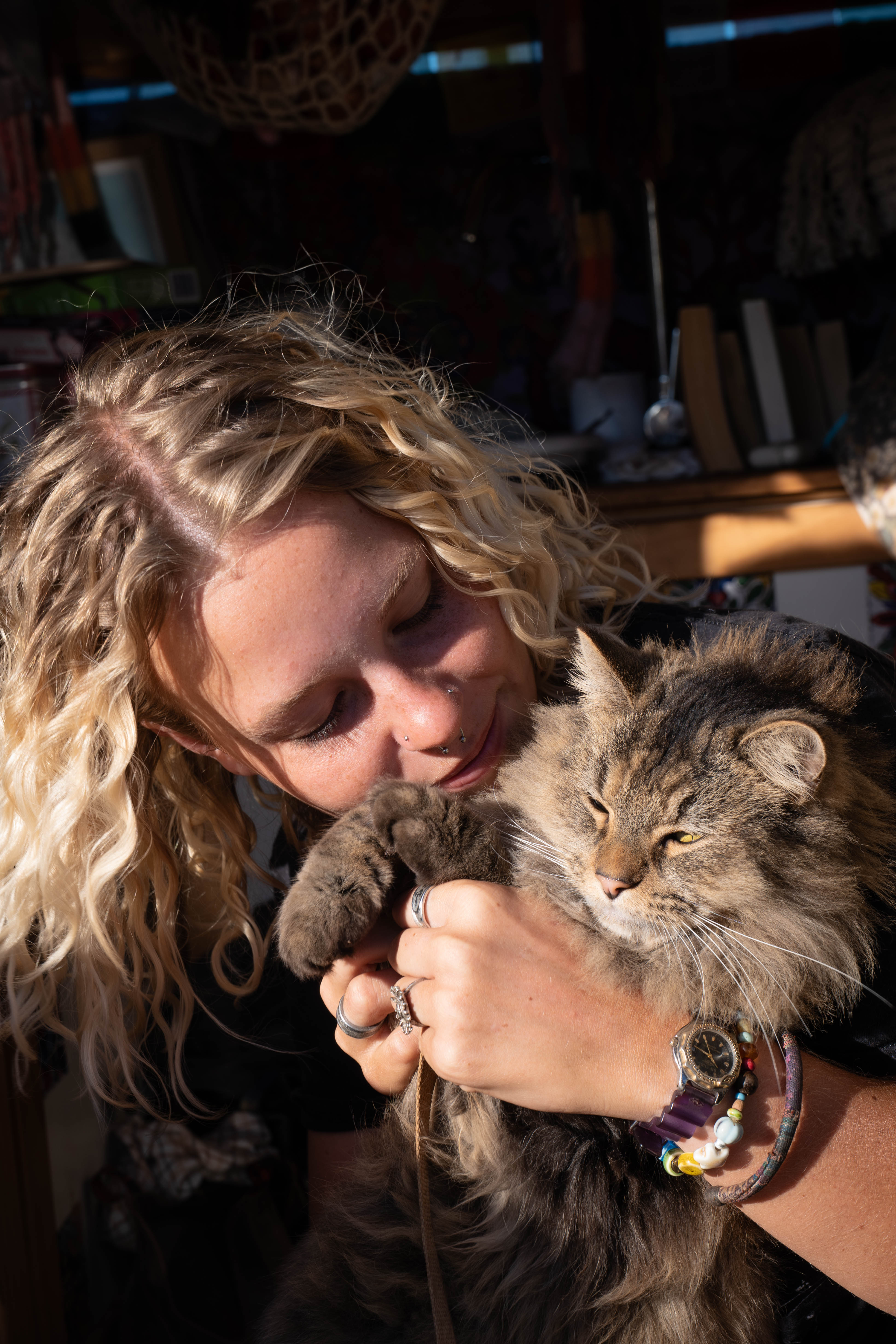 A woman cuddling a long-haired tabby cat in a sunlit room